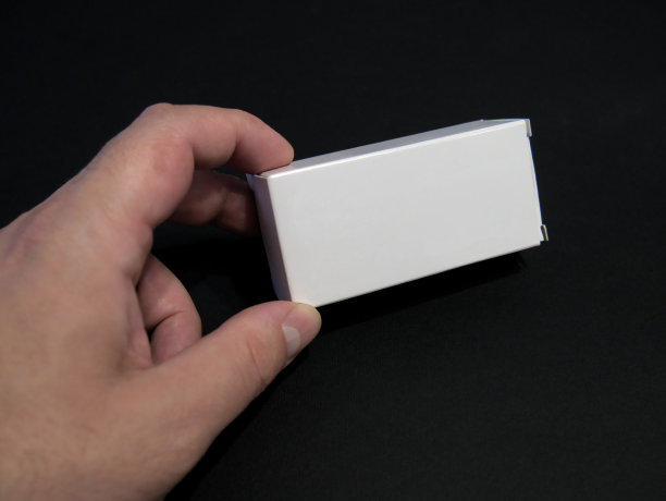 一个人的手拿着白色的小盒子对着黑色的背景，为模拟图片下载