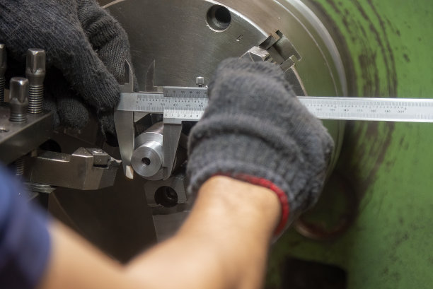 拉近操作人员用游标卡尺测量金属轴零件的场景。图片下载