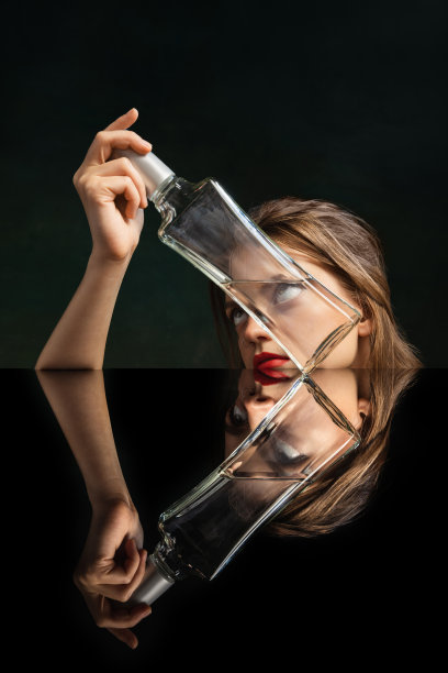 超现实的艺术摄影。年轻女孩的脸透过空玻璃瓶在黑暗的背景。物体变形，光学错觉。当代艺术品。图片下载