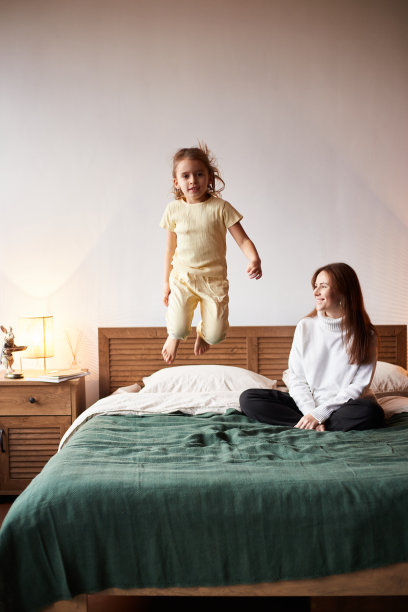 白人小女孩和妈妈玩得开心。圣诞节早上在床上蹦蹦跳跳。阖家欢乐圣诞理念图片下载