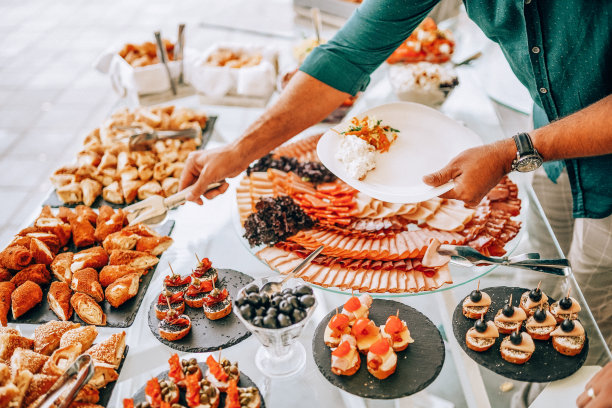 在酒店吃早餐时，手拿餐盘并从自助餐桌上取食的男子图片下载
