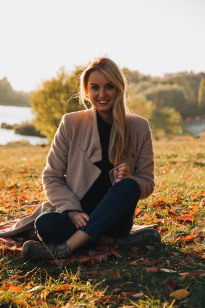 美丽的女孩与金色的长发在秋天的风景在日落。秋天一个女孩坐在草地上的肖像，选择性聚焦图片下载