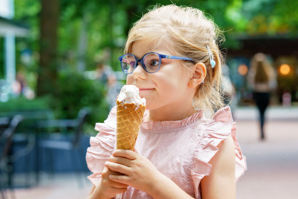 一个学龄前的小女孩，在阳光明媚的夏天，戴着眼镜吃着华夫饼筒里的冰淇淋。快乐蹒跚学步的孩子吃冰淇淋甜点。在炎热温暖的夏天吃甜食图片下载
