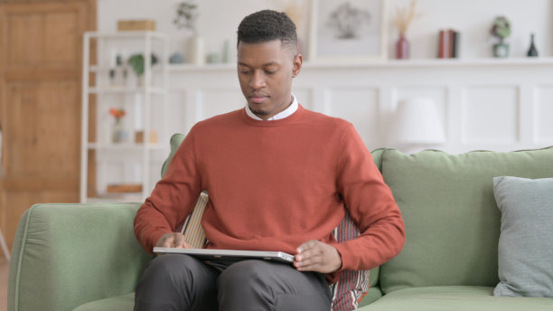 非洲男子坐在沙发上，打开笔记本电脑图片下载
