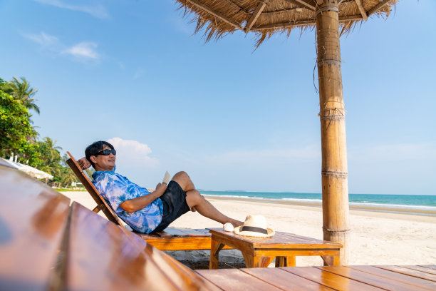 亚洲老人暑假在沙滩上玩电子平板电脑。图片下载