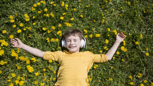 音频愈合。冥想。节奏缓慢的生命。享受小事情。春天的梦。一个戴着耳机的小男孩躺在春日的草地上听音乐图片下载