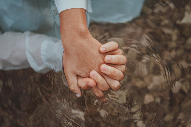 一对穿着衣服的夫妇手牵手在海里。高质量的照片图片下载