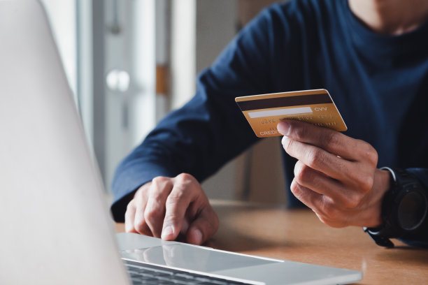 男人手里拿着信用卡，在家里使用笔记本电脑，商人或企业家工作，网上购物，电子商务，网上银行，消费的概念。图片下载