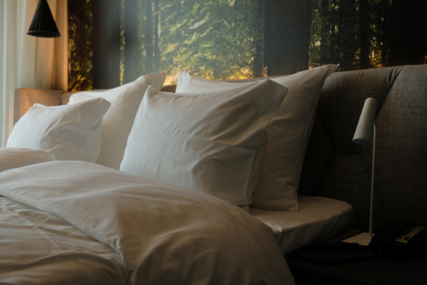 现代室内设计家居或酒店中的卧室碎片与床头柜、阅读灯和插座。柔软的枕头和毯子，时尚舒适的家具。深色的墙壁和房间，选择性的聚焦。图片下载