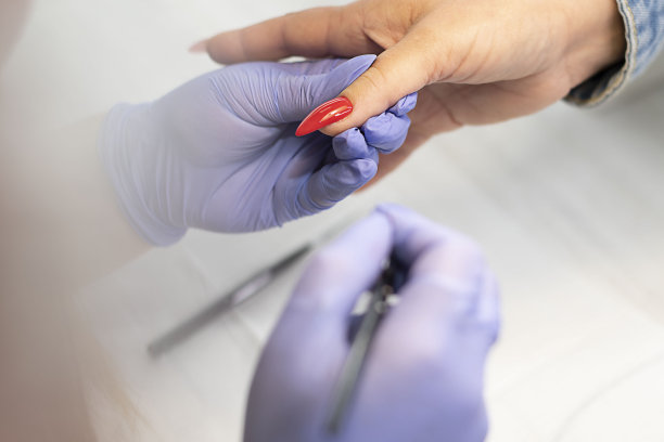 在美容院，戴着乳胶丁香花手套的美甲师在给客户的长指甲上光油。图片下载