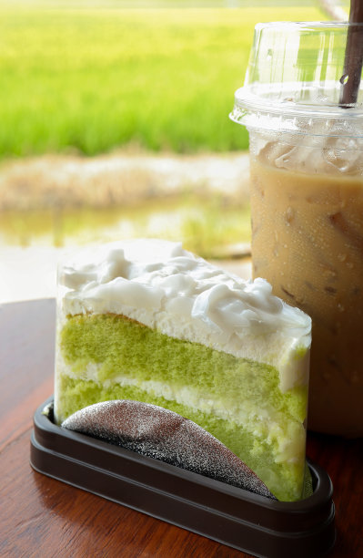 美味的绿色雪纺蛋糕或椰子香兰蛋糕搭配冰咖啡在桌子上。以稻田为背景的咖啡和甜点。图片下载