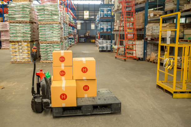 仓库货物箱与手动托盘车或仓库库存产品库存的仓储物流背景。大型工业工厂货架上存放产品的零售盒子。图片下载