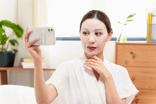 年轻美丽的亚洲女子在家中戴着面膜自拍。图片下载