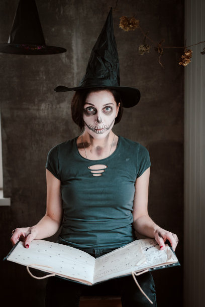 在万圣节，一个穿着女巫服装、化着骷髅妆的女人为女巫打开了一本黑色咒语书图片下载