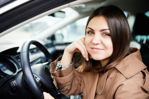 迷人的年轻女子微笑着看着相机，同时开着她的新车去上班图片下载