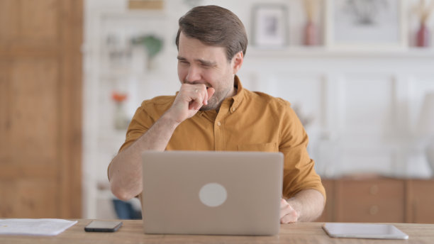 年轻男子在办公室使用笔记本电脑时咳嗽图片下载