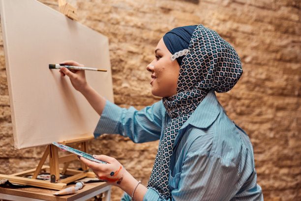 一名戴着头巾的妇女用画笔和蛋彩画在画布上作画图片下载