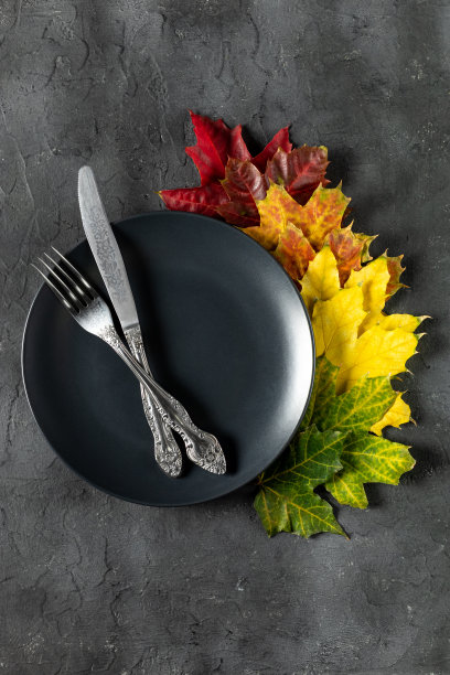 秋天的餐桌设置明亮的彩色树叶和黑色盘子。平的。图片下载