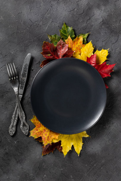 秋天的餐桌设置明亮的彩色树叶和黑色盘子。平的。图片下载