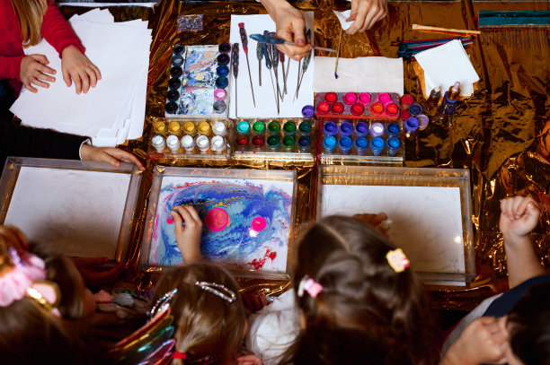 快乐的孩子。俯视创意照片的小男孩和女孩在桌子上画在纸上的颜料一起图片下载