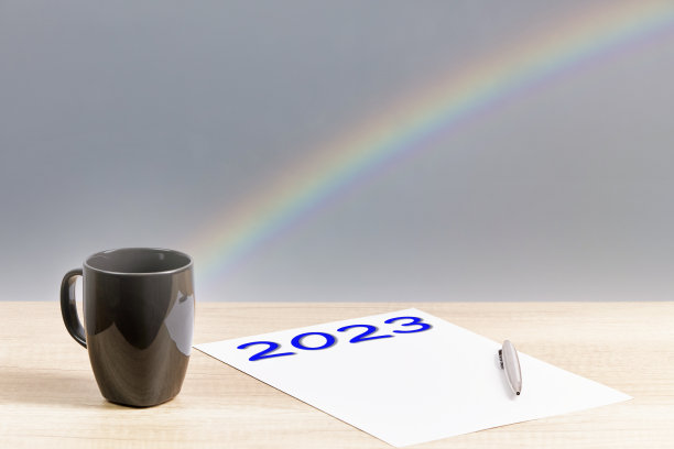 数字2023写在一张纸上，有一个马克杯、一支笔和彩虹背景。新的一年图片下载
