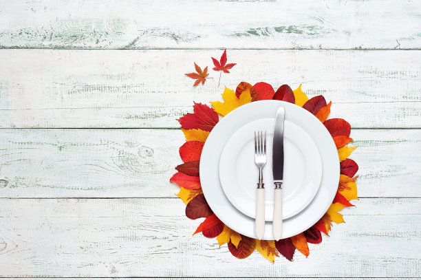 用树叶装饰的木桌上摆放着盘子和餐具素材图片