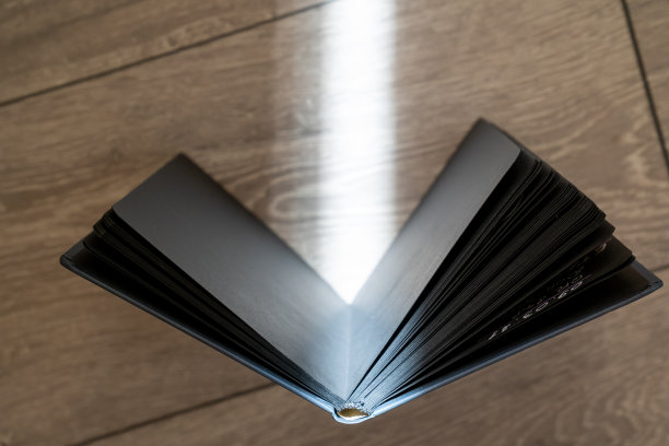 在木制背景上打开课本，黑色的书页，创造阳光光线的效果线条。咒语书的魔法食谱，童话。黑魔法的女巫配件。阅读的过程图片下载