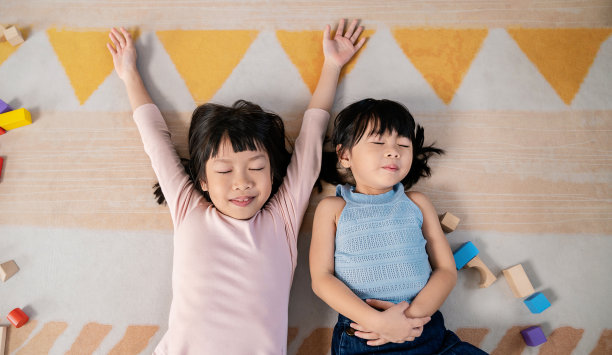 画像年轻快乐的小蹒跚学步的亚洲兄弟姐妹两个小女孩的脸睡在地板上。幼儿教育，姐妹生活方式回到学校一起的理念图片下载