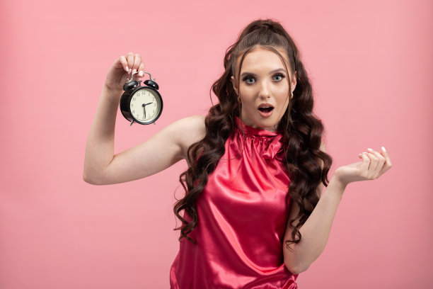 画像一个震惊惊讶的女人跑晚了，拿着一个黑色的时钟在一只手孤立在一个生动的粉红色背景图片下载