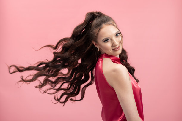 穿粉色衣服的女孩。肖像的微笑可爱的年轻女士玩长黑色的头发扎在马尾洗发水商业彩色背景图片下载