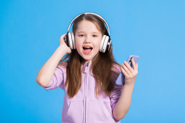 女孩可爱的小孩戴着耳机听音乐。蓝色背景。你最喜欢的歌手唱的歌。最好的免费音乐应用程序为您的移动设备。喜欢的声音图片下载