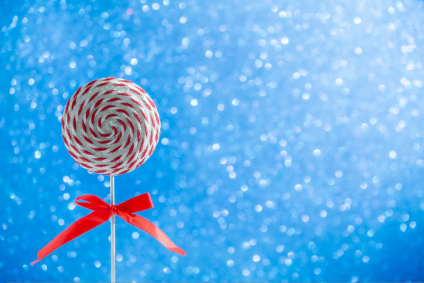 圆形的棒棒糖，红色和白色螺旋。硬糖焦糖，棒棒糖在闪闪发光的蓝色背景。圣诞节的概念图片下载