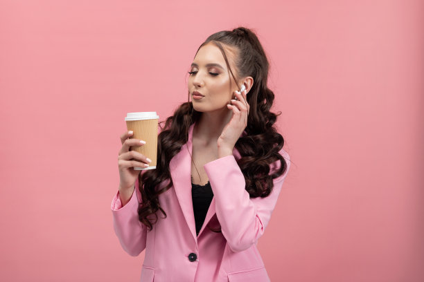 严肃的女人穿着优雅的夹克听着音乐无线耳机一边放松一边喝着咖啡走，闭上眼睛，力量化着妆，梳着发型图片下载