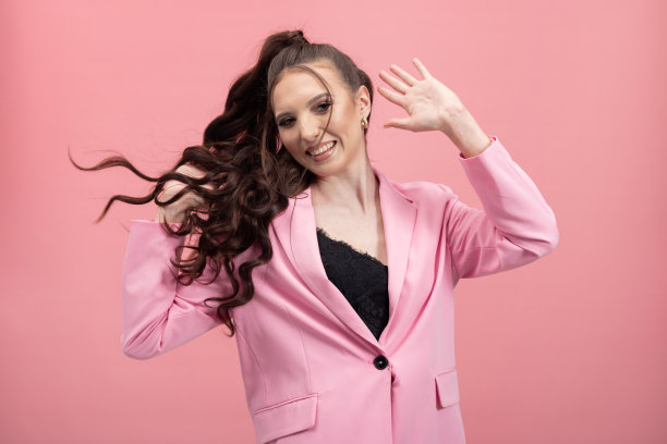 穿粉色衣服的女孩。肖像的微笑可爱的年轻女士玩长黑色的头发扎在马尾辫在彩色的背景图片下载