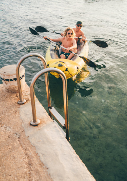 父亲带着十几岁的儿子坐在亮黄色的充气皮艇上，晚上从克罗地亚的西贝尼克市附近的亚得里亚海港口划船回来。度假和家庭价值观垂直形象。图片下载