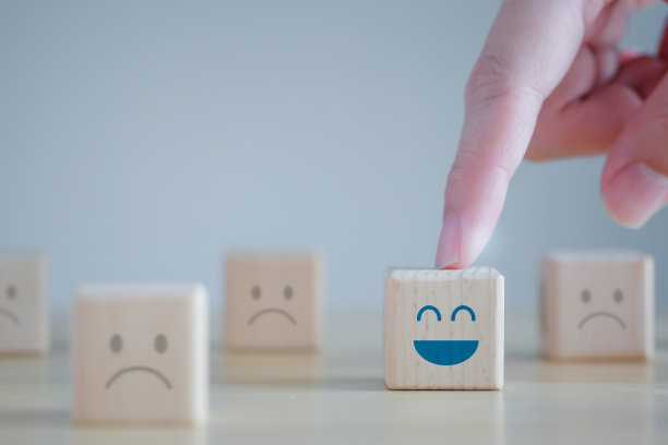 用手指着木块上不快乐的面孔中的快乐的面孔。积极思考、反馈、满意度、客户服务审查、精神健康评估、世界精神卫生日概念。图片下载