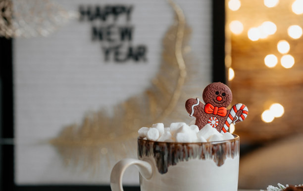 一个写着“新年快乐”的牌子，一个装有热可可、棉花糖的马克杯，一个姜饼人以美丽的黄色焦景为背景。一个温馨的圣诞和寒假概念。图片下载