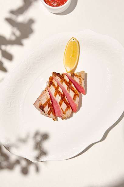 在光线背景和阴影下烤金枪鱼牛排。白桌子上的柠檬烤金枪鱼。与烤鱼排的美学组合。金枪鱼烧烤牛排。烤鱼。夏季菜单。图片下载