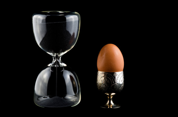 沙漏计时器，鸡蛋装在蛋杯里，放在深色桌布上图片下载