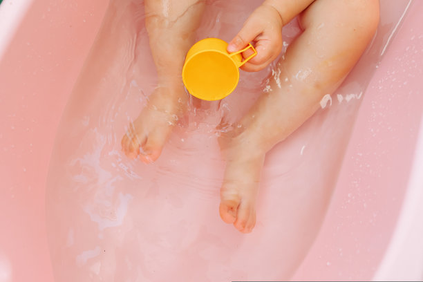 近无法辨认的顶部视图的婴儿脚在一个粉红色的婴儿浴水。图片下载