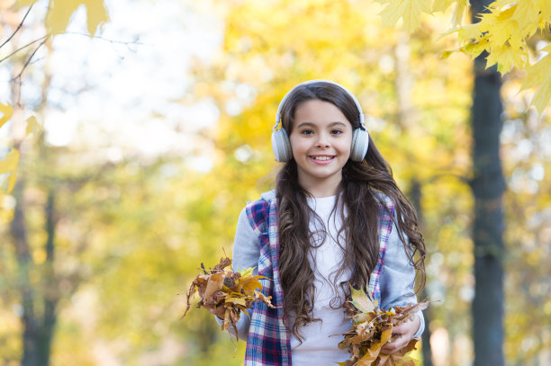 完全自由的感觉。快乐的孩子戴上耳机。十几岁的女孩在上学的路上听音乐。孩子们走在秋天的森林里。秋天的枫叶。在线教育童年的幸福。美和自然图片下载