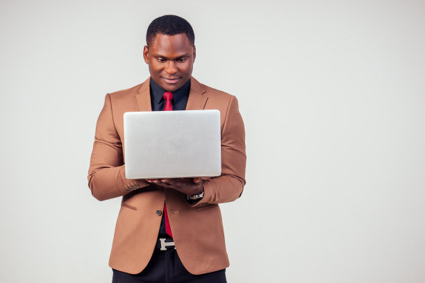 英俊的非洲裔美国人，穿着经典的西装，微笑着在白色背景的演播室里使用笔记本电脑图片下载