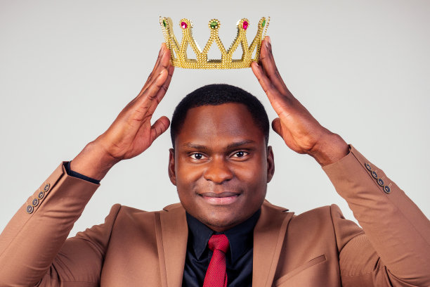 聪明的非裔美国成功和富有的商人在时尚的西装和他的头上的金色皇冠在白色背景的工作室拍摄。值得尊重和幸运的概念图片下载