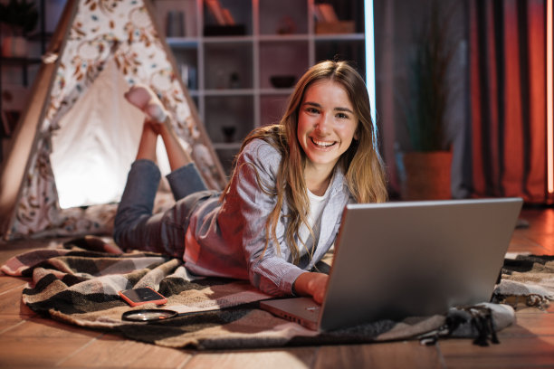 漂亮可爱的年轻女孩在宿舍外面的地板上在家里使用笔记本电脑。图片下载