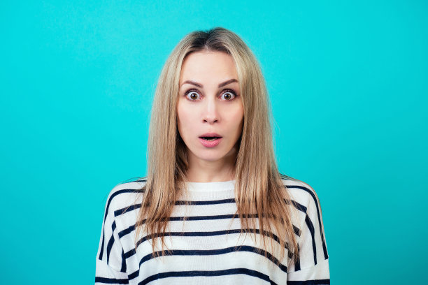 一个年轻的有吸引力的震惊的女人与金发和化妆的嘴在工作室的蓝色背景打开惊讶的肖像。惊奇和令人惊叹的新闻的概念图片下载