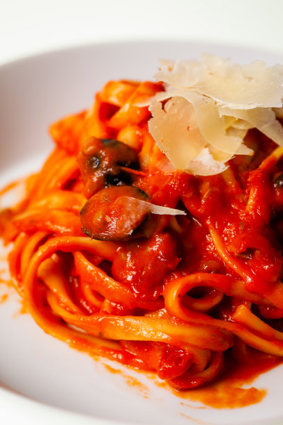 特写照片的意大利面与番茄酱和一个白色盘子的部分视图，意大利面与番茄酱和橄榄在一个白色背景上的盘子。图片下载