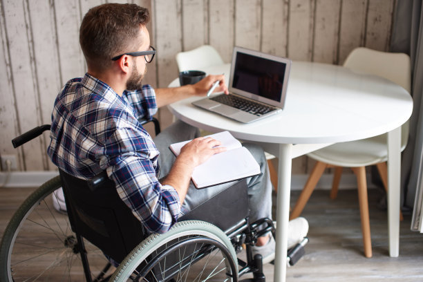 残疾青年在使用笔记本电脑时用记事本做笔记图片下载