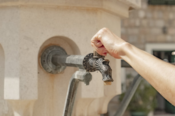 一个女孩用手打开街边的水龙头喝水。一个老水龙头，街上有水。图片下载