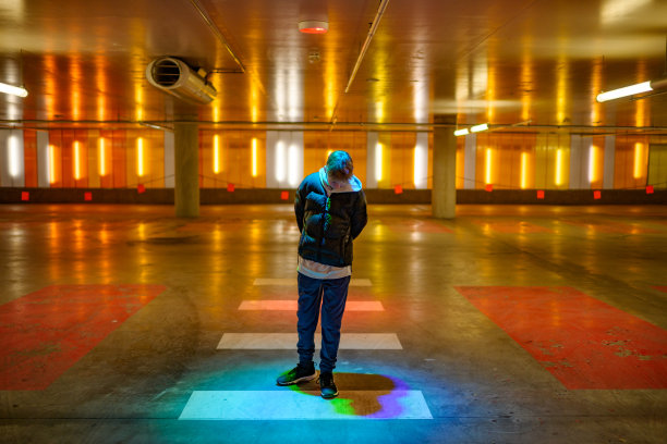 十几岁的男孩走在一个明亮的停车场向下看五颜六色的影子图片下载