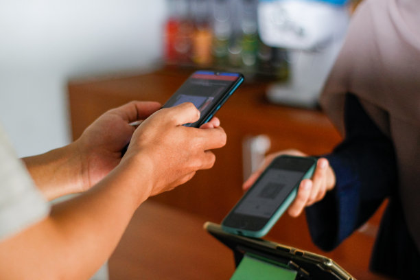 年轻的亚洲男子在咖啡馆购物。他正在用智能手机支付，在刷卡机上扫描并支付账单，实现了快速、简便的非接触式支付图片下载